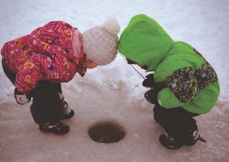two children looking down an ice fishing hole